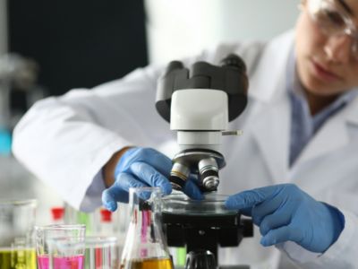 Scientist examining samples under a microscope in a laboratory, representing ALS drug development research